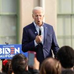 Man speaking at an outdoor event with Biden sign.