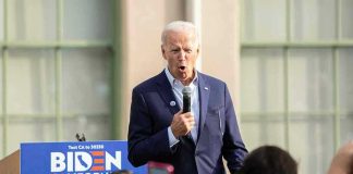 Man speaking at an outdoor event with Biden sign.