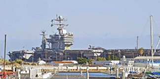U.S. Nuclear Warship Arrives In Caribbean Amid Cuba Standoff A large naval aircraft carrier docked in a harbor with smaller boats in the foreground