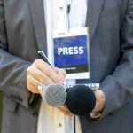 Press member holding microphones and taking notes.