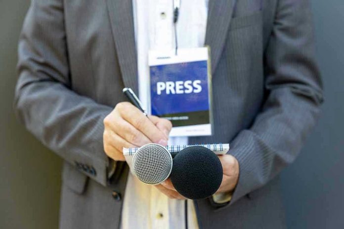1808083621 Press member holding microphones and taking notes.