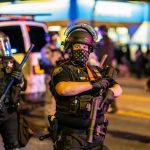 Police officer in riot gear holding a weapon at night