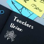 A black notebook with 'Teachers Union' written on it, surrounded by colorful sticky notes and paper clips