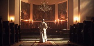 A religious figure standing in a church with candlelight and historic artwork