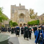 Graduates and faculty in academic regalia walking on a university campus