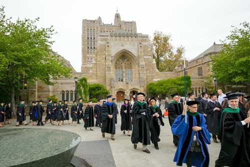 Graduates and faculty in academic regalia walking on a university campus