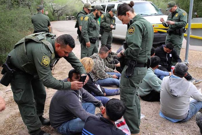 Law enforcement officers process a seated group outdoors