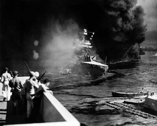 shutterstock_239397877 A naval ship engulfed in smoke and flames with military personnel observing from a distance