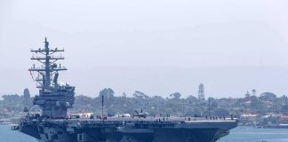 Aircraft carrier escorted by a tugboat in a harbor