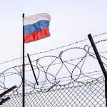 Russia Strikes Deal to Keep Military Foothold in Post-Assad Syria Russian flag behind barbed wire fence