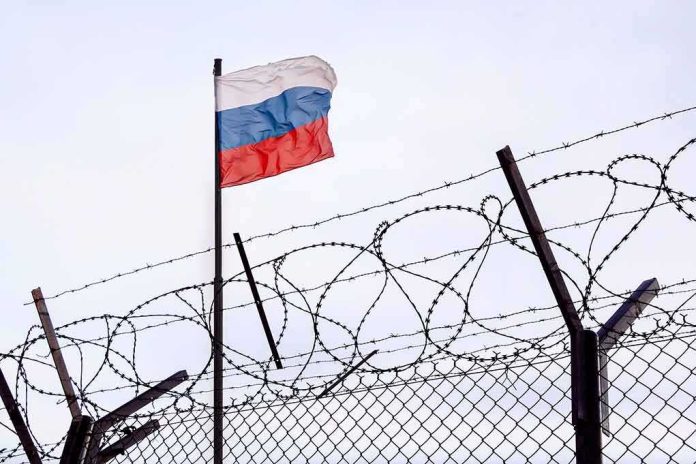 shutterstock_2156169421 Russian flag behind barbed wire fence
