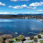 Aerial view of a lakeside town with pier and boats under a blue sky