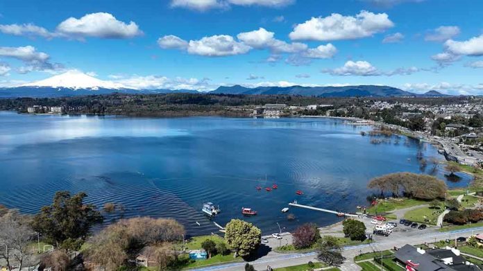 shutterstock_2363571211 Aerial view of a lakeside town with pier and boats under a blue sky