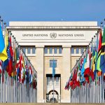 Nuclear Near-Miss Warning Shocks UN United Nations building with numerous national flags outside.