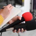 Trump Envoys Go From PUTIN Straight to Zelenskyy Journalist holding two microphones while writing in a notebook
