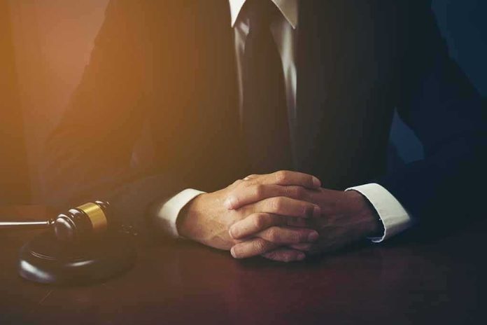 person in suit with hands clasped at a desk beside a gavel