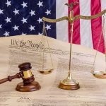 Scales of justice and gavel on the U.S. Constitution with American flag backdrop