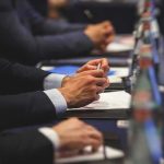 Hands of people in suits taking notes at a conference table
