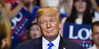 Donald Trump at a rally wearing a dark suit and blue tie