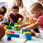 Karyn Polito with toddlers building blocks on a play mat