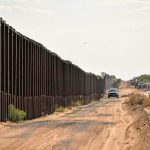 Border fence beside a dusty desert road with trucks