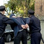 police officers arresting a person against a wall outdoors