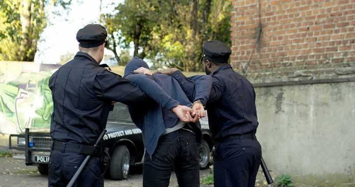 shutterstock_1716453646 police officers arresting a person against a wall outdoors