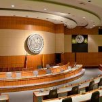 DOJ Exposes Victims, Shields Power Players Interior view of a government chamber with wooden paneling and seating