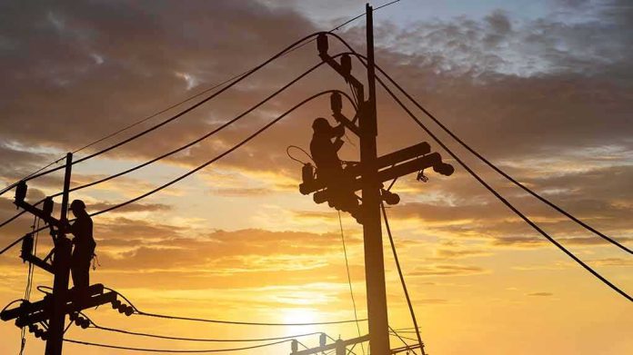 Utility workers on power poles at sunset