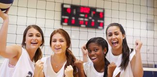 High School Athlete SHAKEN About Locker Room Situation Four female volleyball players celebrate by the net in a gym