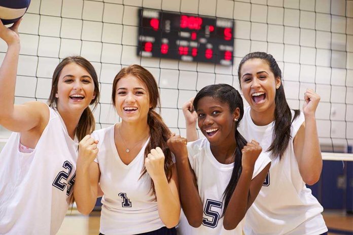 shutterstock_199091366 Four female volleyball players celebrate by the net in a gym