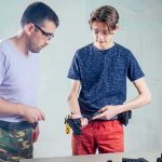 Two people at a table handling a handgun with safety glasses on