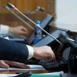 Iran War Hype—Budget Explodes In The Trillions Person pressing a button on a conference microphone panel