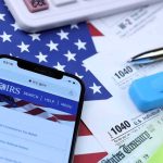 Smartphone showing IRS website on top of tax forms and office supplies