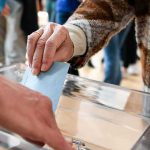 Hand inserting ballot into transparent box