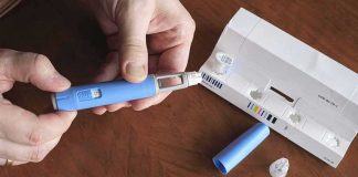 Hands assembling a blue insulin pen with packaging on a table