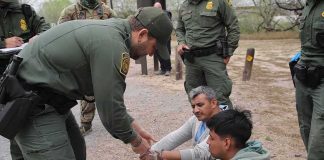 law enforcement officer handcuffing two seated men outdoors