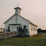Church Massacres Are Being Ignored — Why? Small white church with steeple and cross at sunset