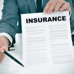 How The Trump DOJ Took On Dominant Hospital System Person in suit holding an insurance document and a pen