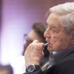 George Soros in profile, holding a pen to his lips during an event
