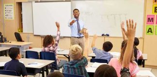 Teacher at front of classroom as students raise hands