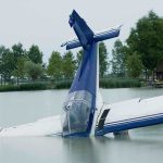 A submerged airplane partially in a lake with trees in the background