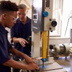 Student operating a bandsaw under instructor supervision