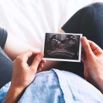 Outrage Erupts Over Diagnosis-Driven Abortion Person holding an ultrasound photo over a pregnant belly