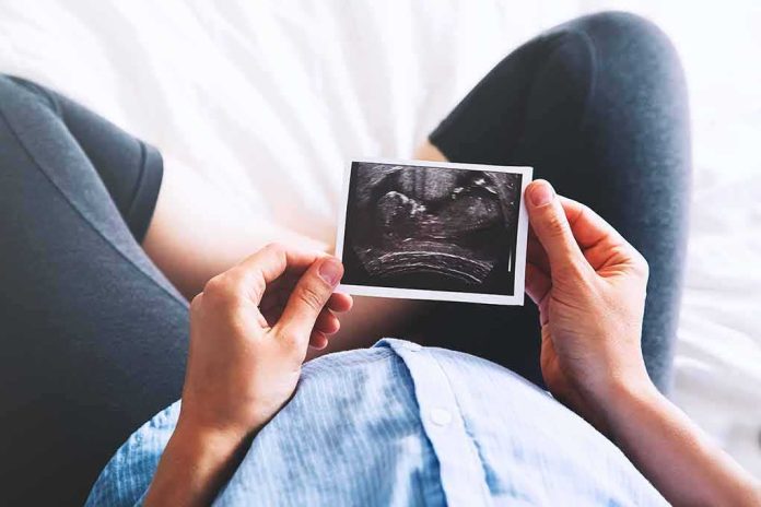 shutterstock_626242508 Person holding an ultrasound photo over a pregnant belly