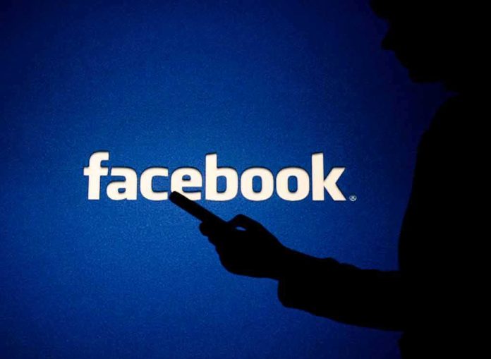 shutterstock_1083574463 silhouette holding a smartphone in front of Facebook logo