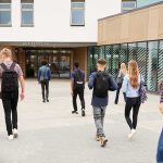 Fake Teacher Taught THREE Classes Students with backpacks walking toward a school entrance