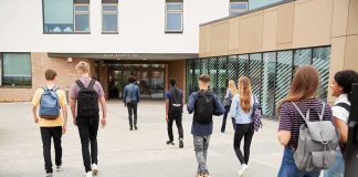 Fake Teacher Taught THREE Classes Students with backpacks walking toward a school entrance
