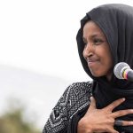 How Ilhan Omar Got So RICH Ilhan Omar speaking at a microphone with hand on chest