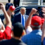 Man in suit greeted by crowd with raised hands